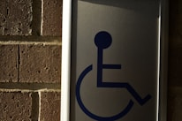A metal sign with a blue symbol of a person in a wheelchair, mounted on a brick wall.