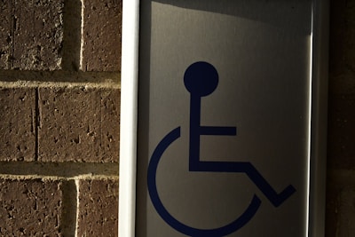 A metal sign with a blue symbol of a person in a wheelchair, mounted on a brick wall.