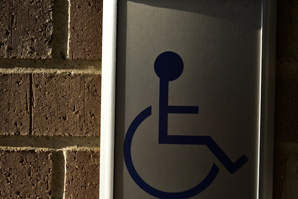 A metal sign with a blue symbol of a person in a wheelchair, mounted on a brick wall.