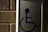 A metal sign with a blue symbol of a person in a wheelchair, mounted on a brick wall.