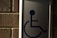 A metal sign with a blue symbol of a person in a wheelchair, mounted on a brick wall.