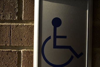 A metal sign with a blue symbol of a person in a wheelchair, mounted on a brick wall.
