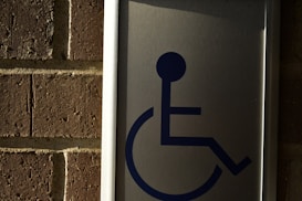 A metal sign with a blue symbol of a person in a wheelchair, mounted on a brick wall.