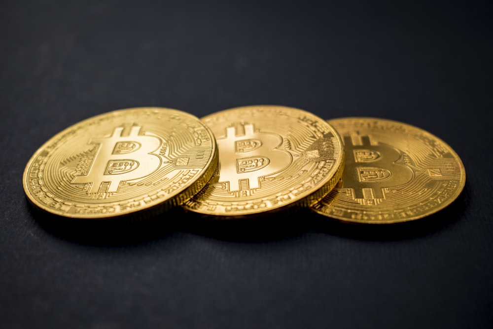 three gold-colored bitcoins on black surface