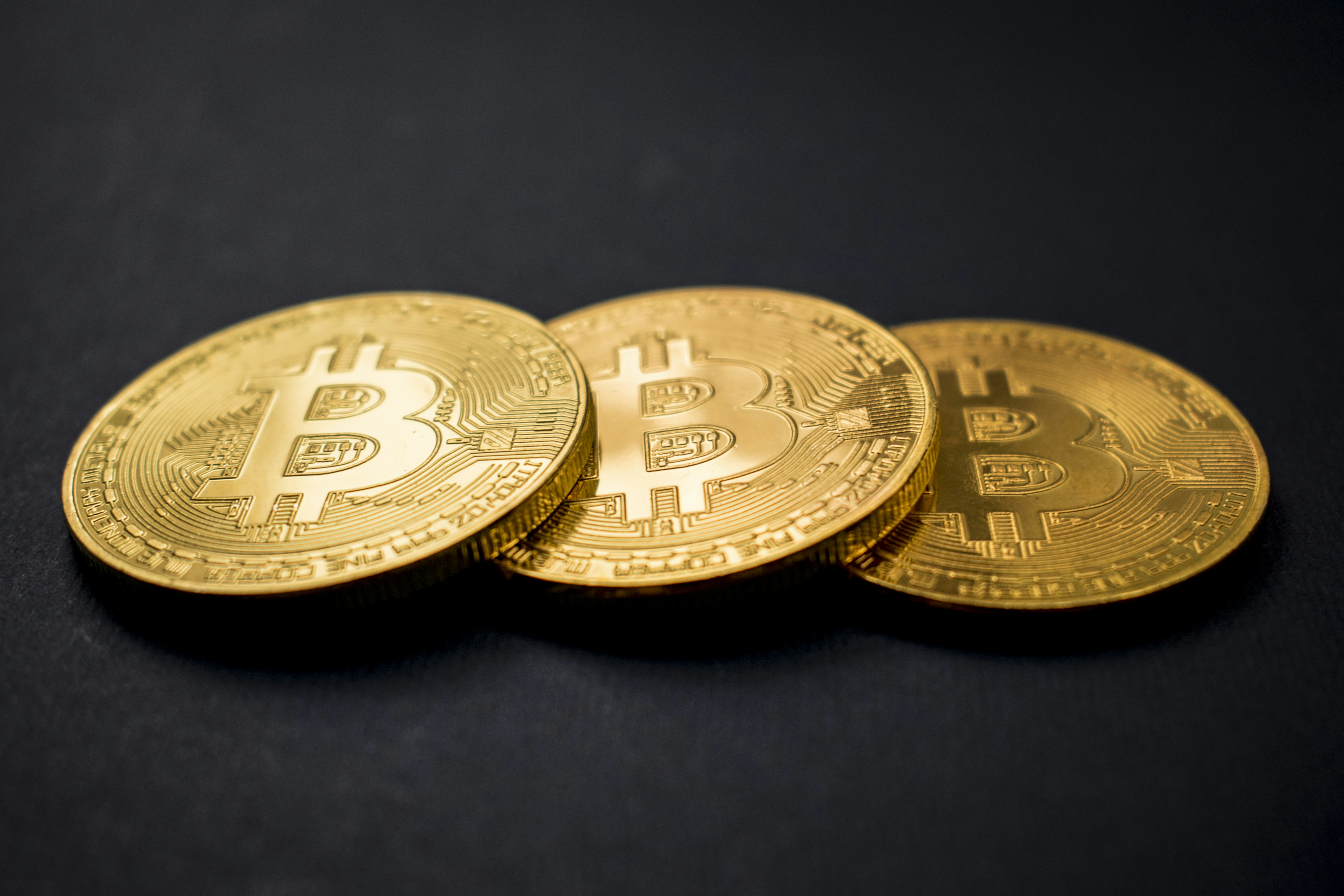 three gold-colored bitcoins on black surface