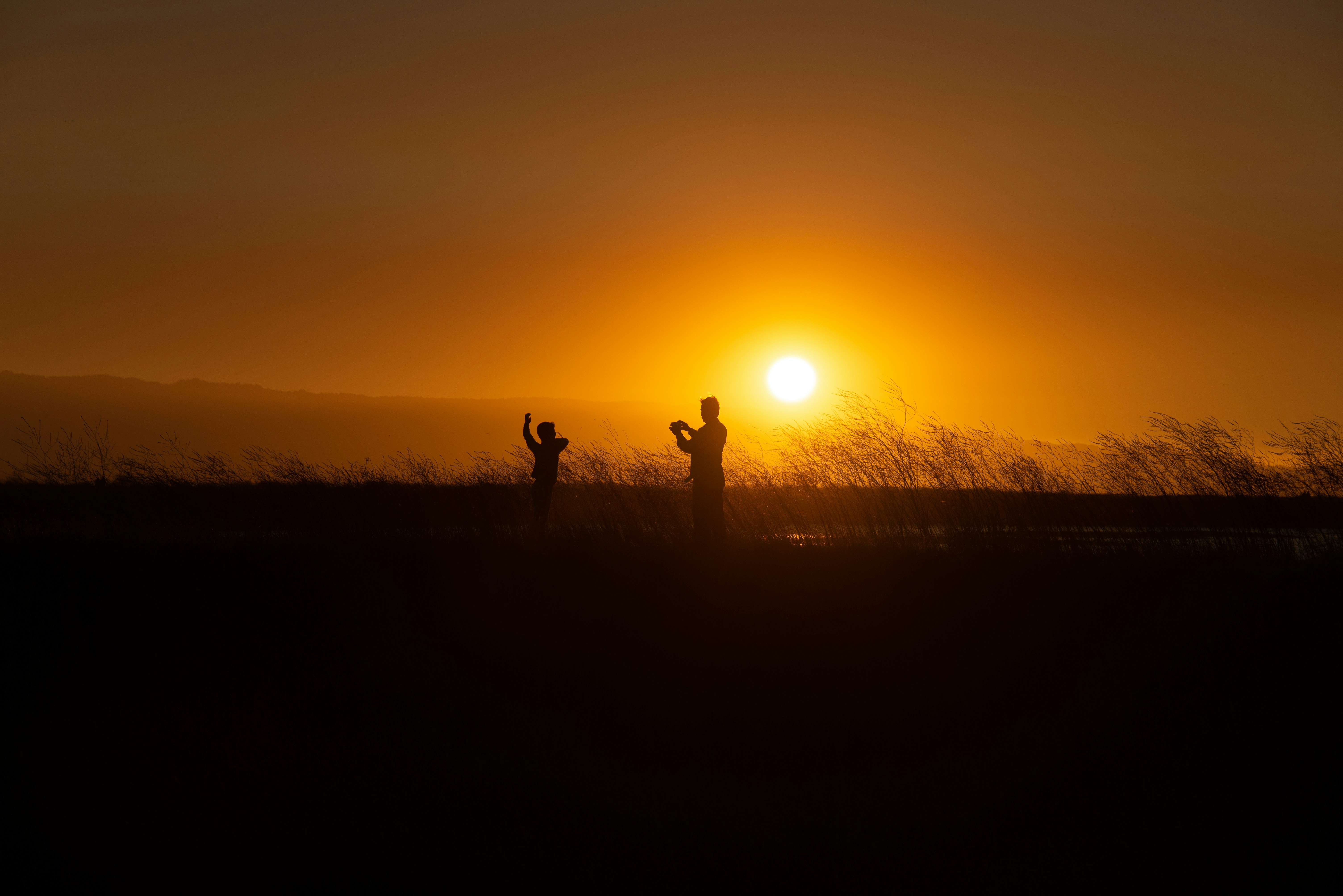 silhouette of two people on grassfield playing under orange sky