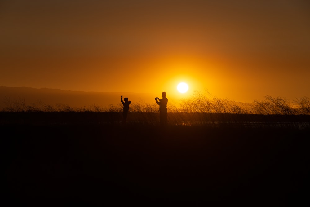 silhouette of two people on grassfield playing under orange sky