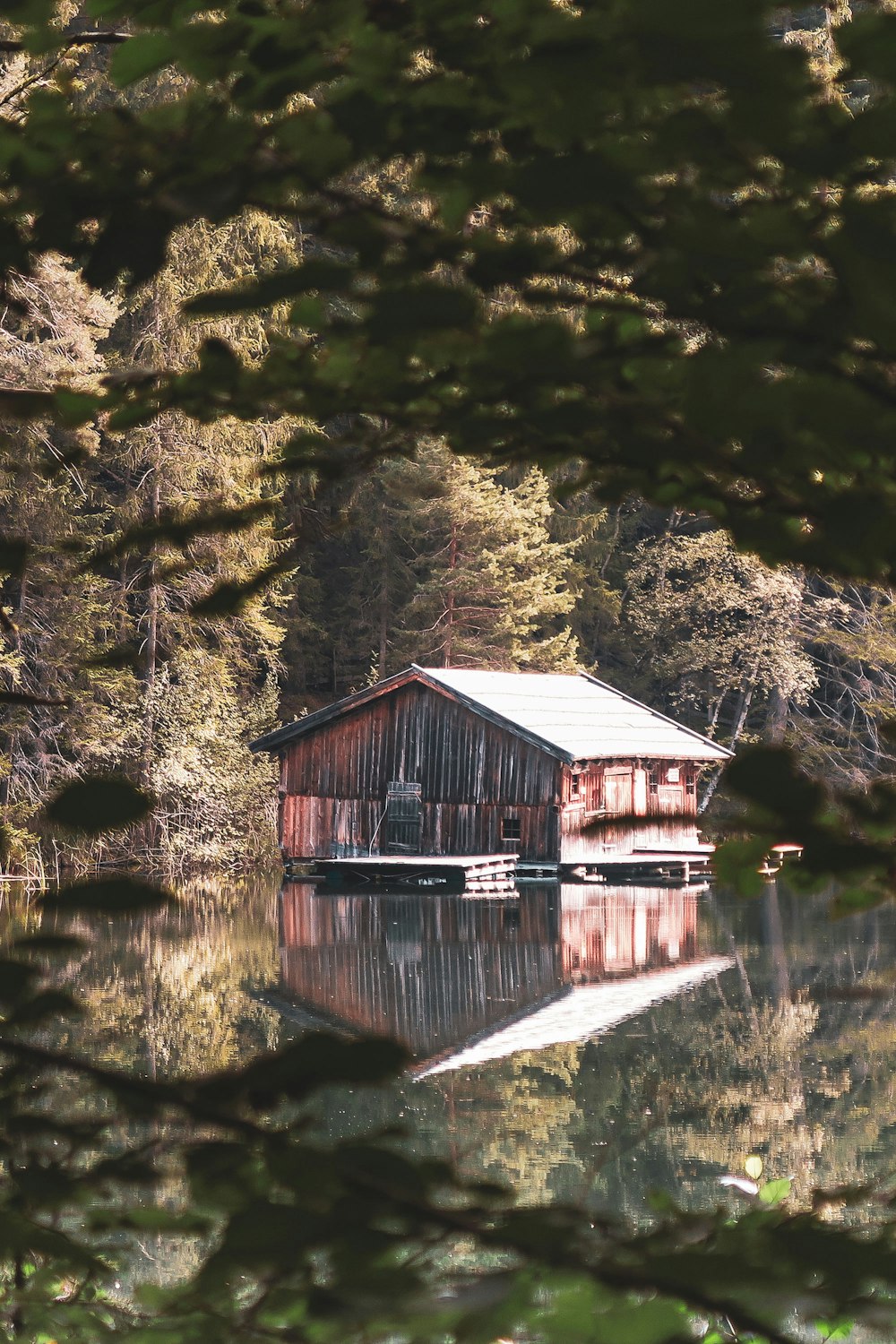 brown wooden house near body of water and trees