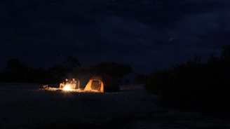 Mike and Sarah sitting by a campfire with their kayak and tent in the background at sunset.