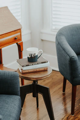 Compact side table holding snacks and a book beside a cozy armchair.