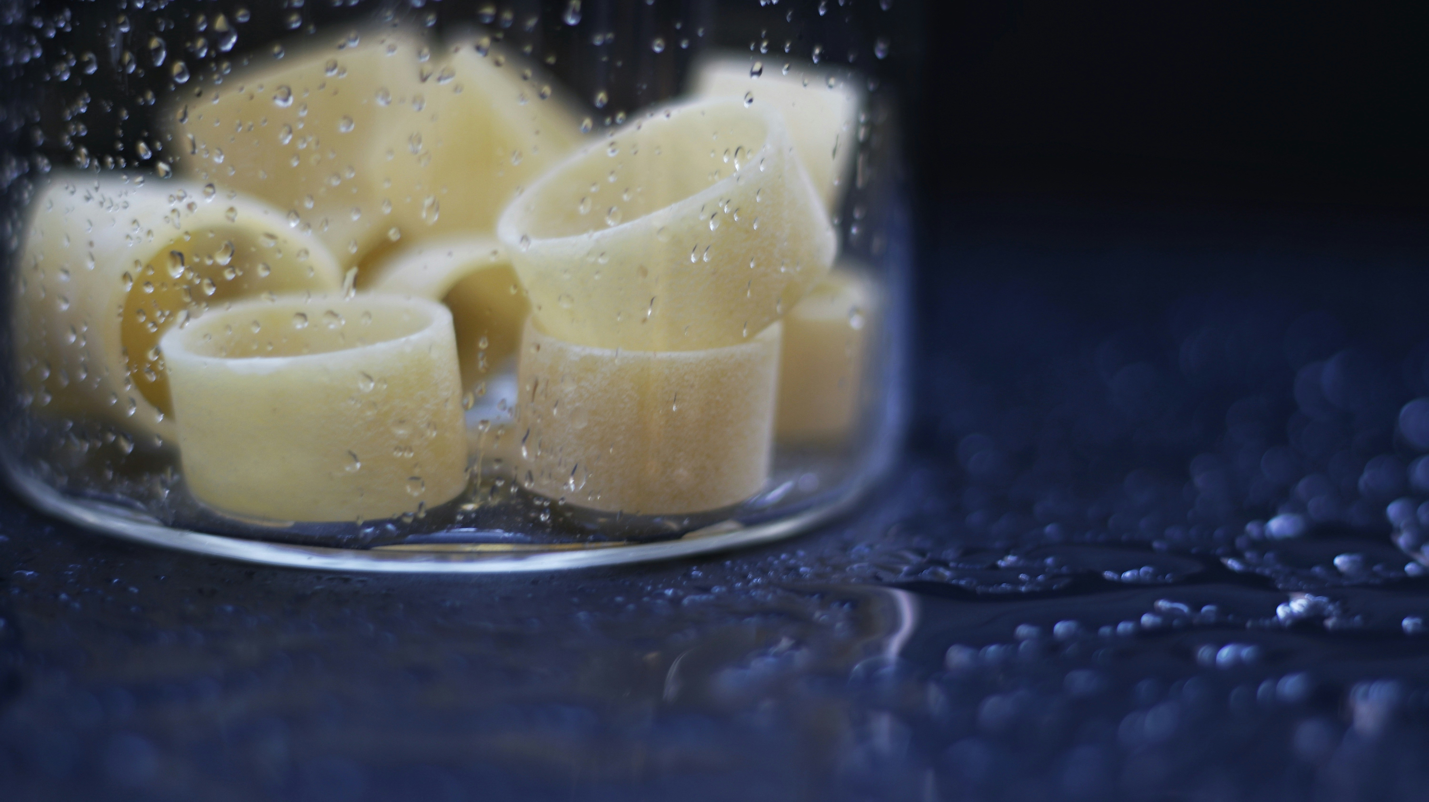 Large tube pasta shapes arranged on dark slate surface, moody product photography, deep shadows, dramatic lighting
