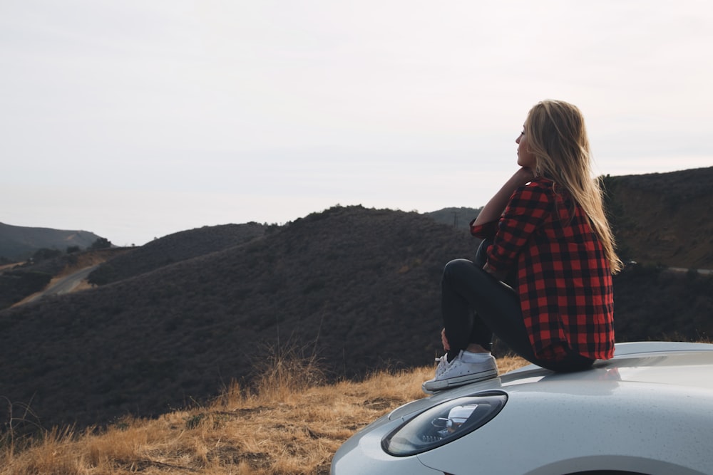 woman in red and black plaid shirt sitting at the hood of car