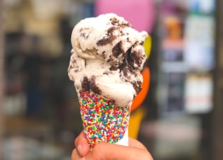 person holding candy sprinkled cone with ice cream