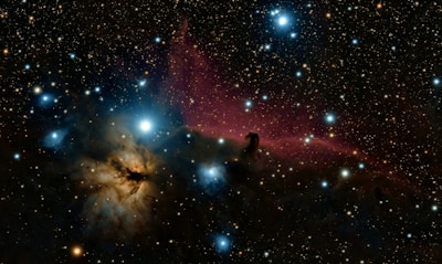 A stunning view of a starry night sky with a large number of bright stars scattered across the image. In the center, a bright blue star stands out among a nebula with purplish and dark blue hues. The nebula is visually captivating with intricate textures and patterns, while darker areas suggest dense cosmic material.