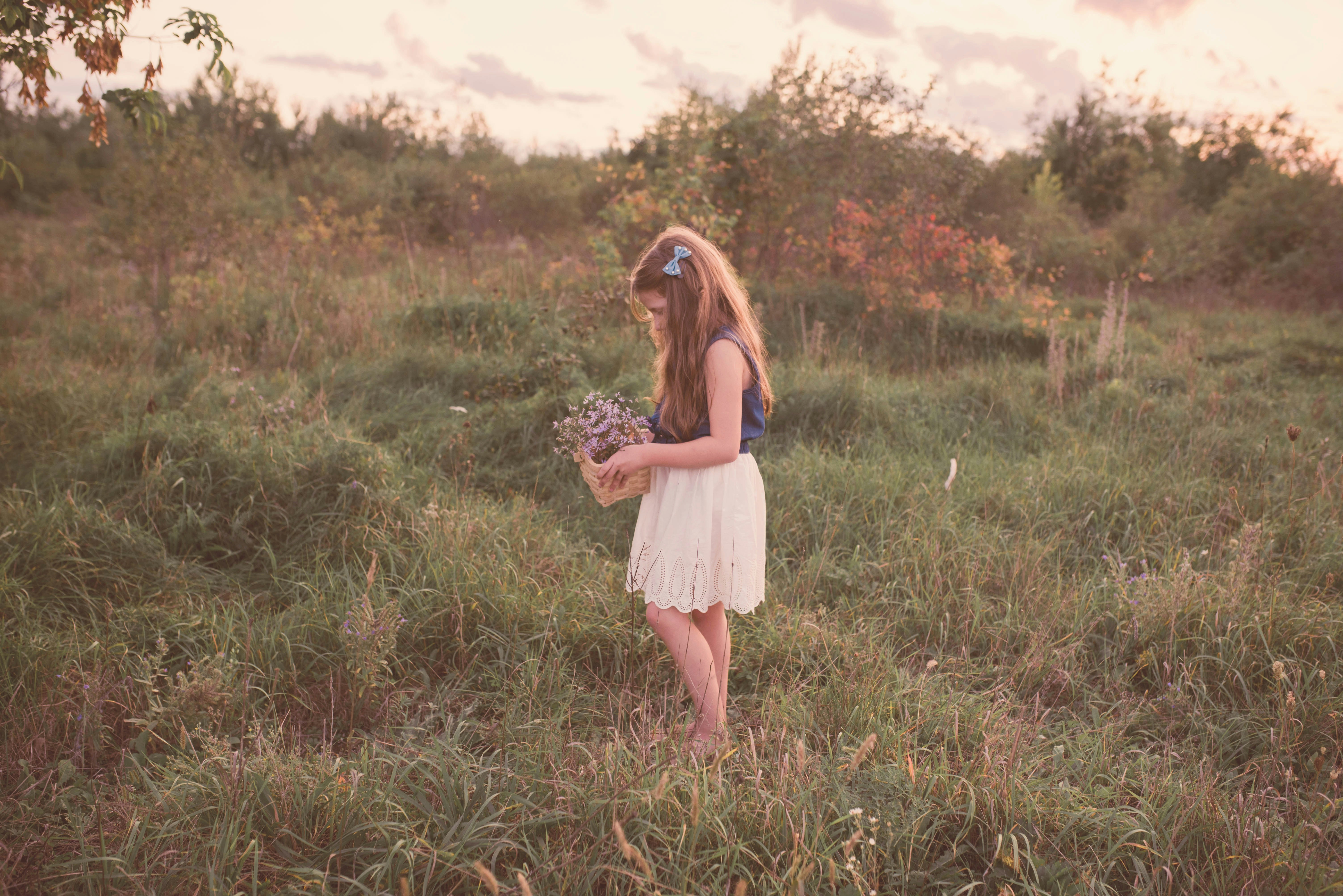 girl holding basket of flower standing on grass field
