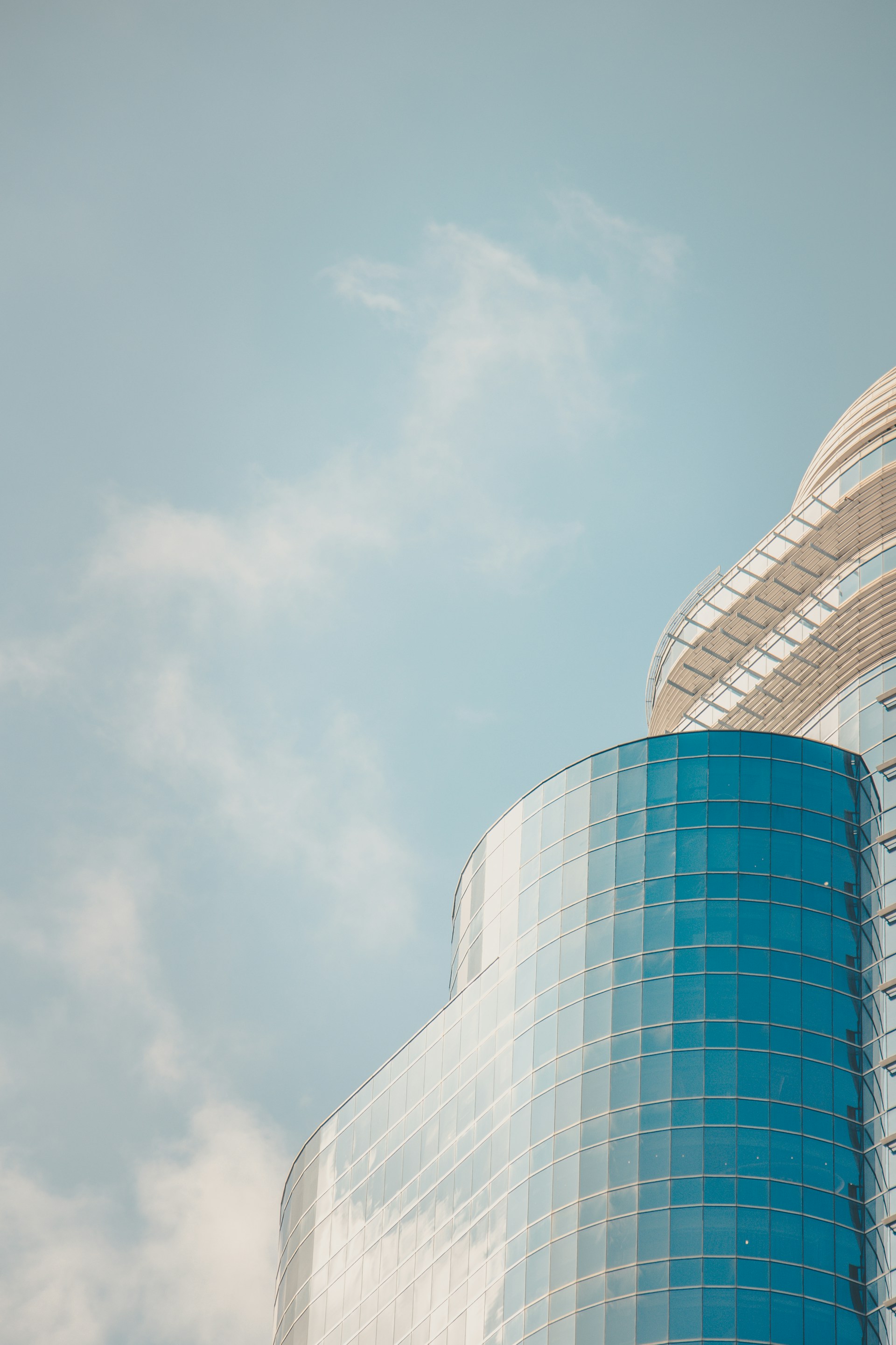 A sleek modern building with glass facades reflecting the sky, captured in soft morning light.