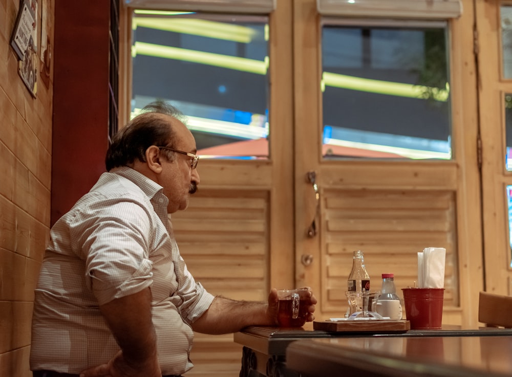 man sitting near the table while holding glass mug