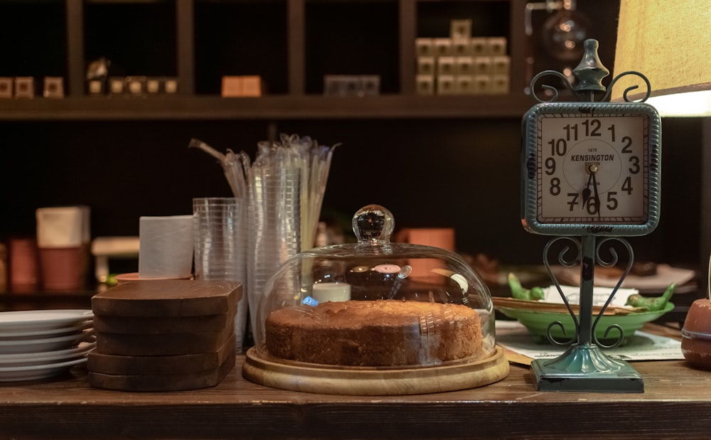 clear glass cake dome beside desk clock at table