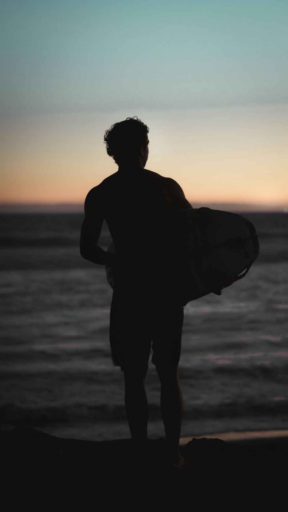 silhouette di uomo in piedi sulla riva che tiene il bodyboard