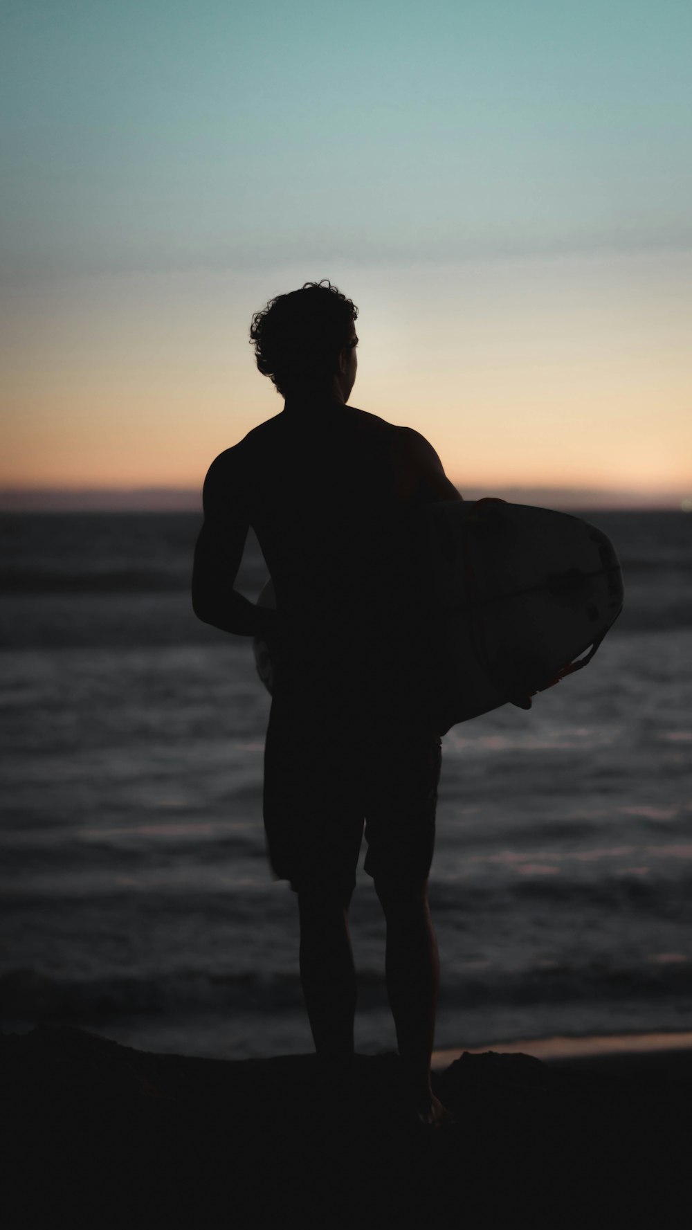 silhouette of man standing on shore holding bodyboard