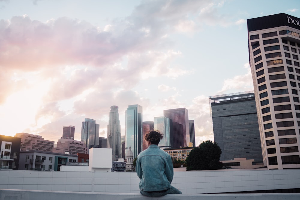 man sitting on ledge facing buildings at daytime