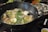 A large black pot filled with a variety of ingredients simmering in broth. Visible ingredients include broccoli, green beans, mushrooms, tofu, and assorted vegetables. The setup suggests a communal dining experience, possibly a hot pot meal.