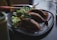 A plate with empanadas and a fresh salad, garnished with a rich sauce, is placed on a dark table. Nearby, there is a smoothie in a glass jar and various utensils.