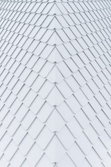 Uniformly arranged white tiles create a geometric pattern with a symmetrical and seamless appearance, resembling a roof or wall surface. The tiles are aligned in diagonal rows, each slightly overlapping the next, forming a repetitive and organized texture.