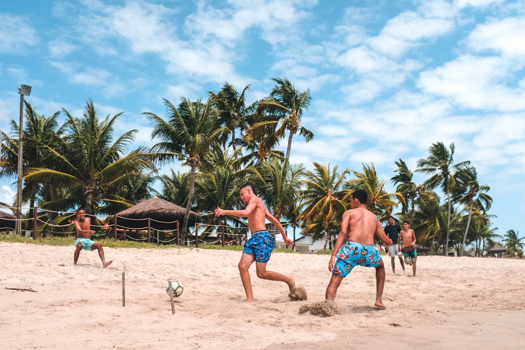 several men playing football on beach sand,