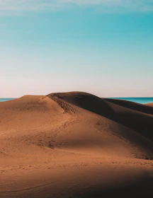 A serene desert landscape with towering sand dunes under a clear blue sky.
