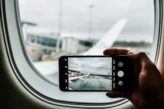 A cheerful traveler using a smartphone to book a flight with a scenic airport background.