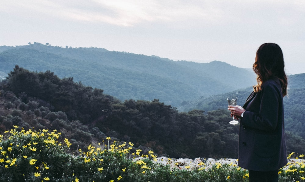 woman standing near flower fields looking at mountain during daytime