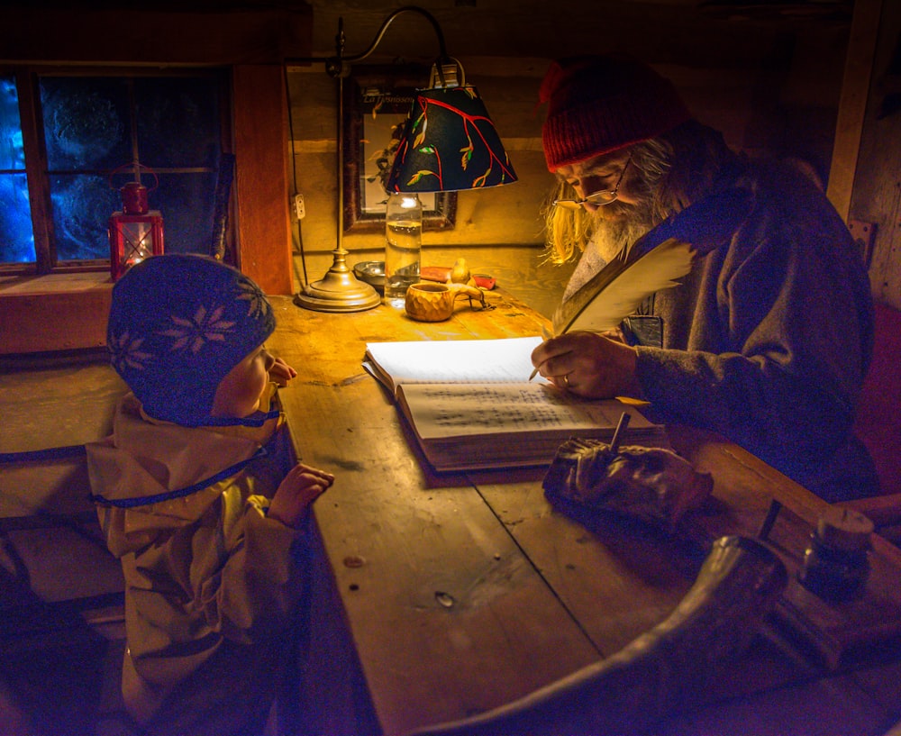 man writing on book near child on table