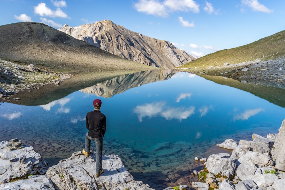 man standing on seacliff facing mountain range