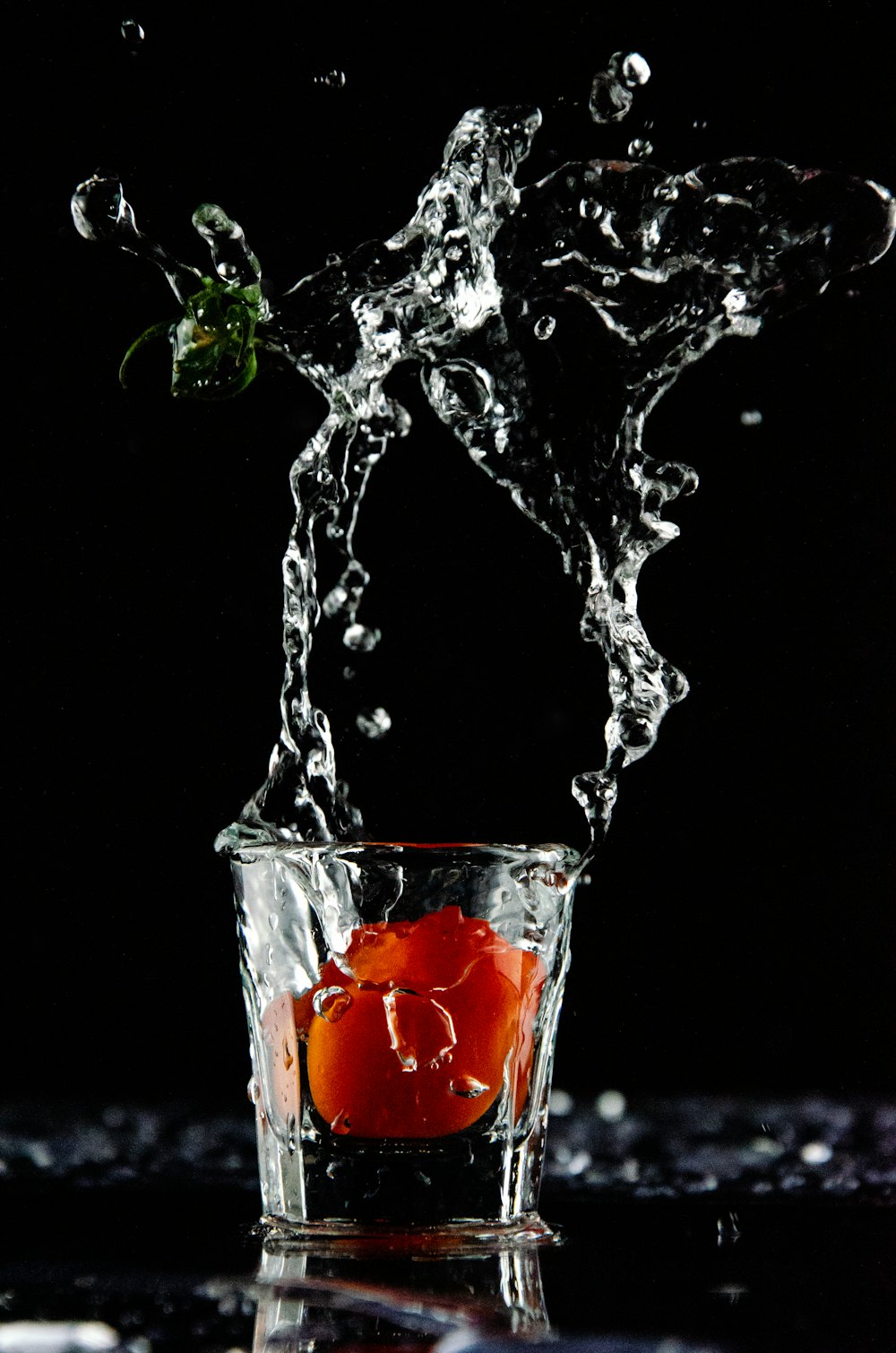 orange fruit dropped on shot glass with clear liquid spills