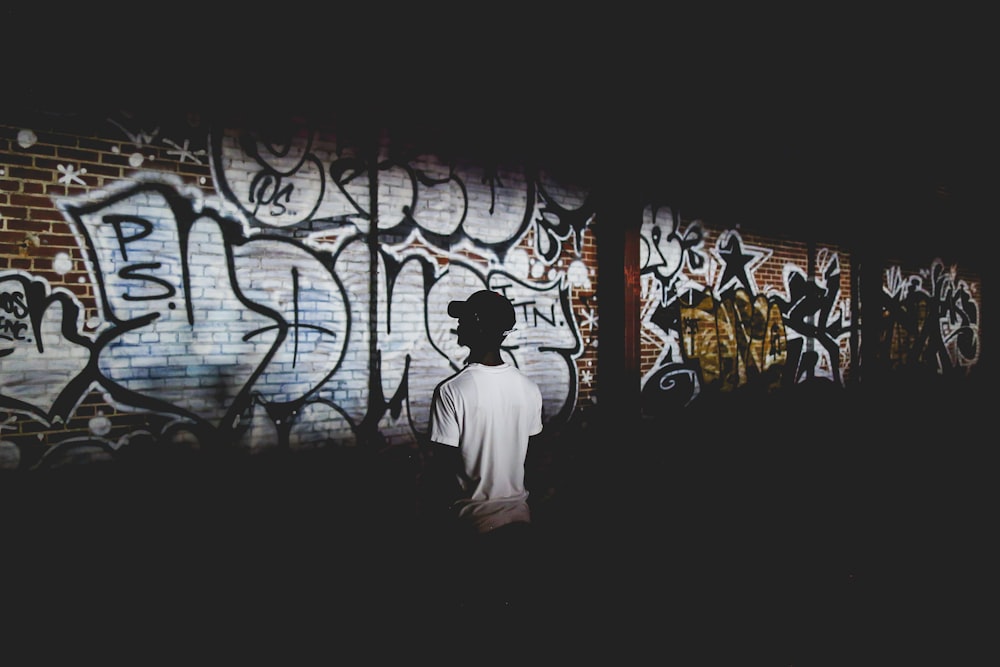 man standing beside wall with graffiti text