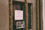 A close-up view of a weathered window protected by rusted metal bars. Inside the window is a white piece of paper with typed text that reads 'BRITTNEY CRUSH LOVES PUERTO RICO.' Below the paper is a sticker with the word 'UBUNTU' in bold typography. The scene suggests a blend of personal expression and urban decay.
