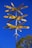 A tall signpost with multiple yellow directional signs pointing towards various cities around the world, mounted on a metal pole. The signpost stands against a clear blue sky, with some trees in the background.