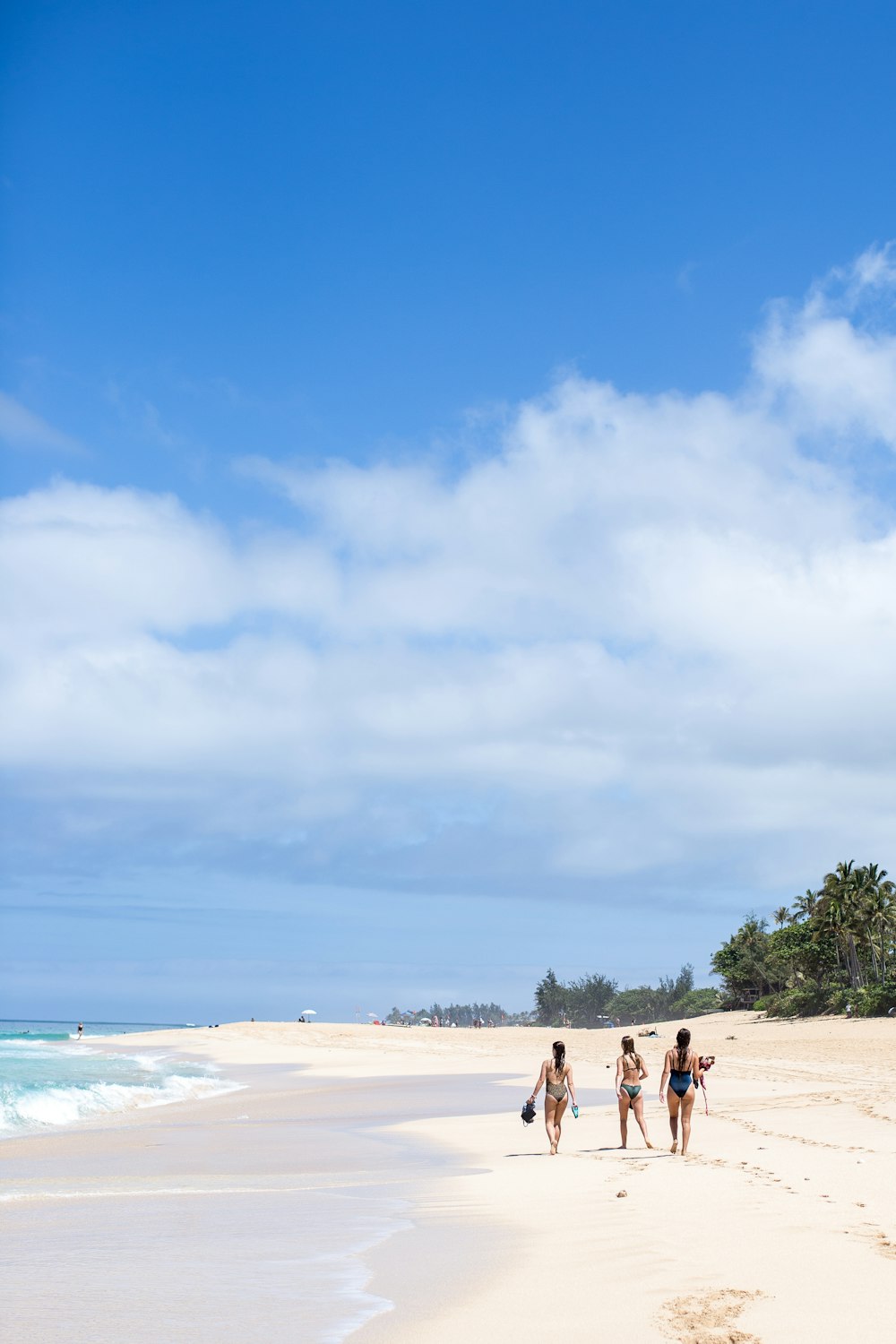 three women on sea shore under blue and white sky during daytime