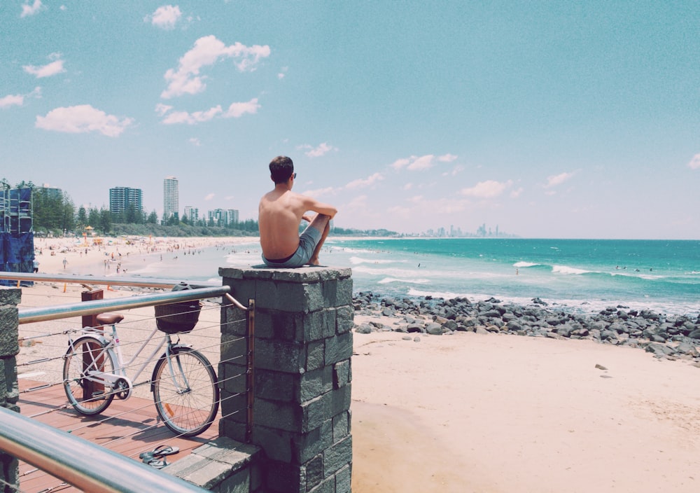 해변을 마주보고 있는 콘크리트 기둥 꼭대기에 앉아 있는 남자