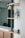 A minimalist interior space with wooden shelves mounted on a wall. A small green plant with long leaves is placed on one shelf, and a small decorative figurine sits on another. The background is softened, emphasizing the clean lines and natural textures of the furniture.