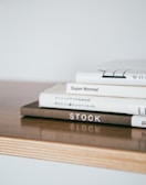 Stack of hardcover books with minimalist covers arranged on a wooden desk.
