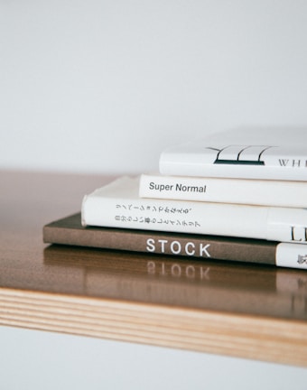 Stack of hardcover books with minimalist covers arranged on a wooden desk.