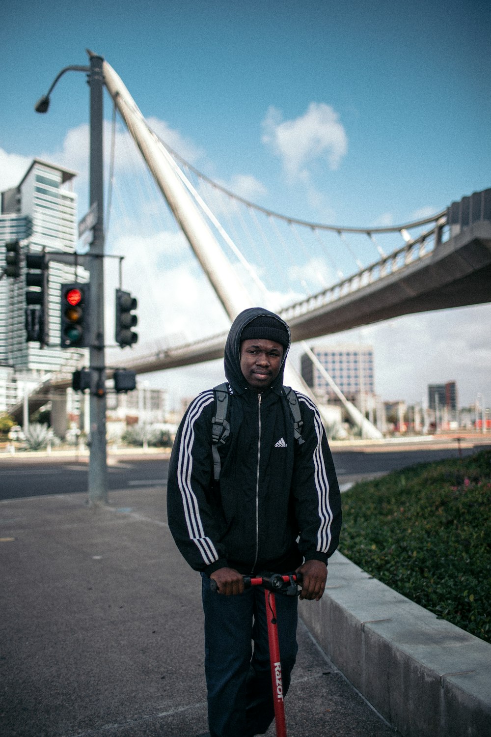 man wearing black and white Adidas jacket riding red kick scooter