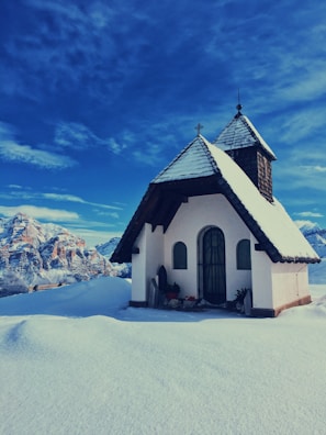 A peaceful chapel surrounded by snow-covered trees under a clear blue sky.