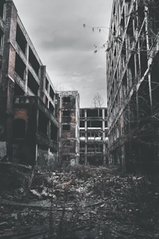 Abandoned brick factory buildings with broken windows and graffiti under a cloudy sky