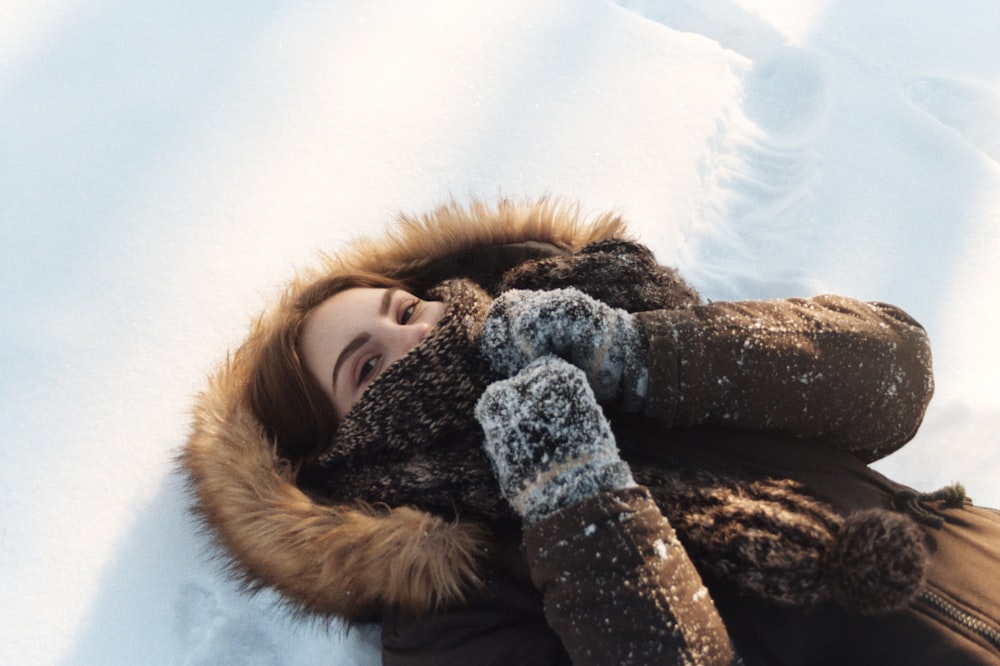 woman in brown fur coat lying on snow