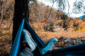 An adventurer relaxing in a Golite hammock with a flowing river beneath and autumn leaves overhead.