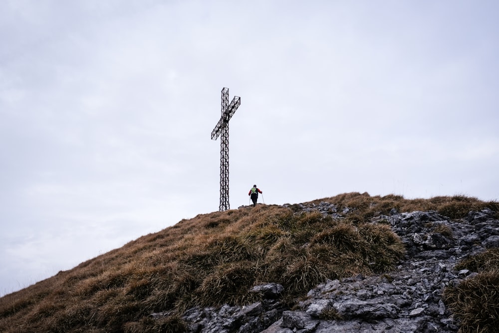 homem caminhando em direção à cruz gigante na colina durante o dia