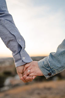 Gilson and Daniely holding hands during a serene outdoor prayer moment, with gentle blue skies behind them.